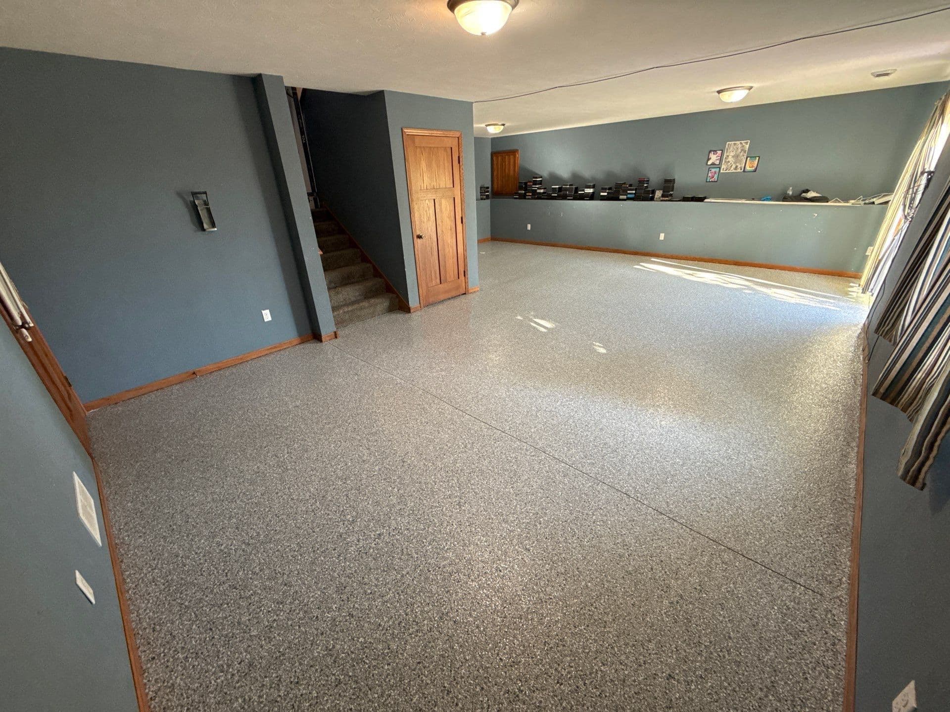 A finished basement with dark blue-gray walls, brown trim, and newly-coated gray flecked polyurea flake concrete flooring.