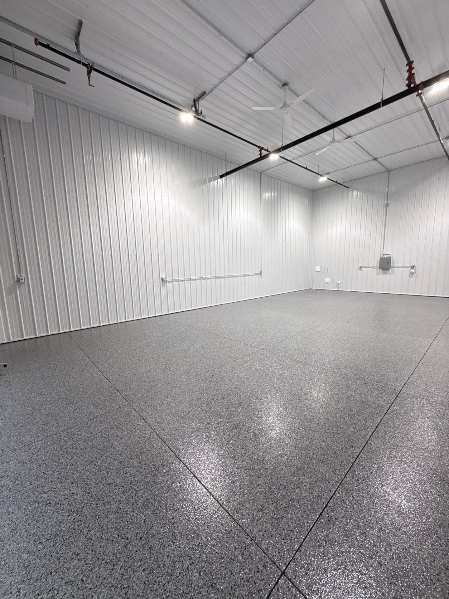 A commercial warehouse space with white metal walls and ceiling, and a newly-coated gray flecked concrete flooring.