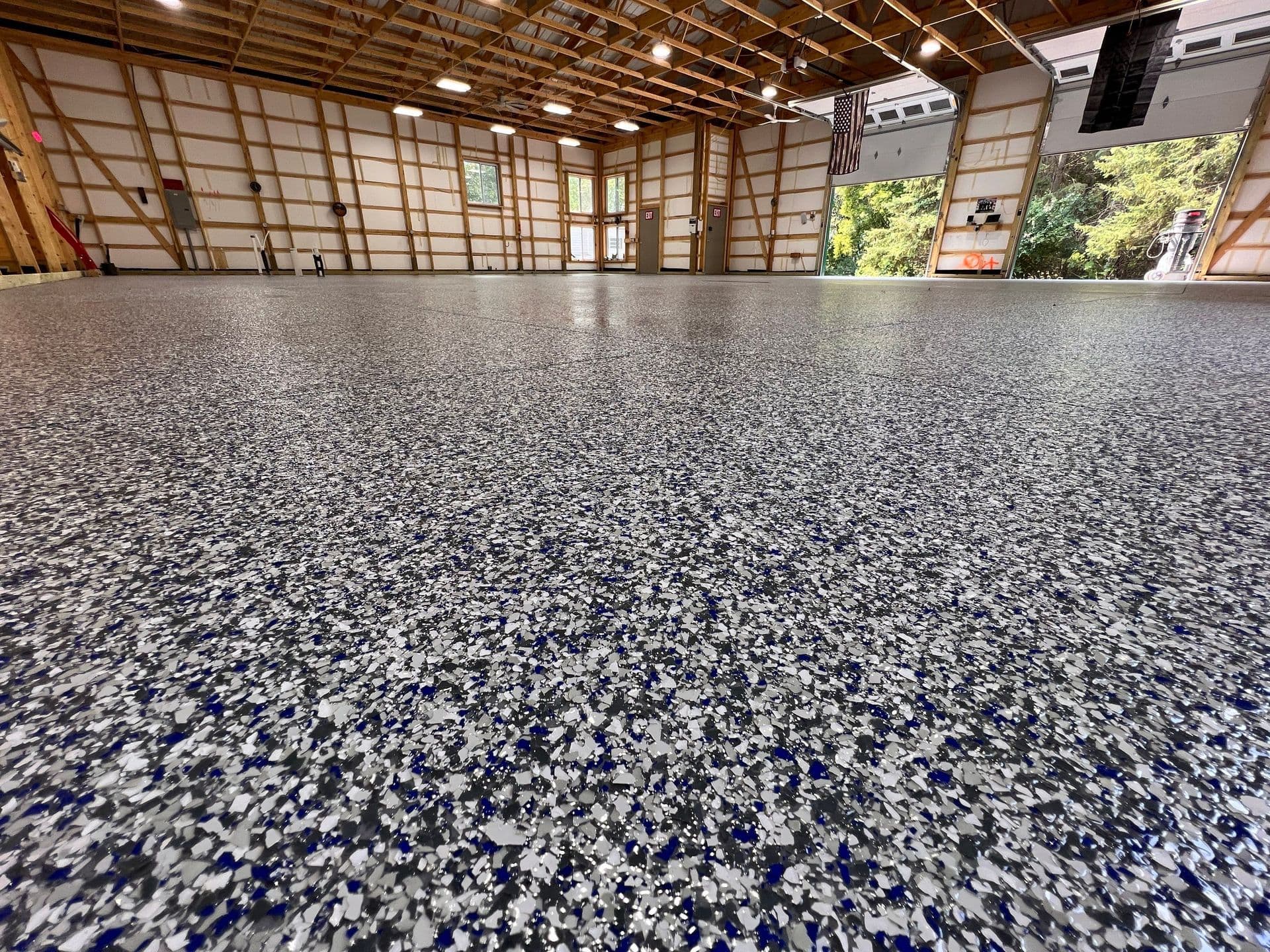 A large garage with multiple bays and newly-coated blue, black, and white flecked flake concrete flooring.