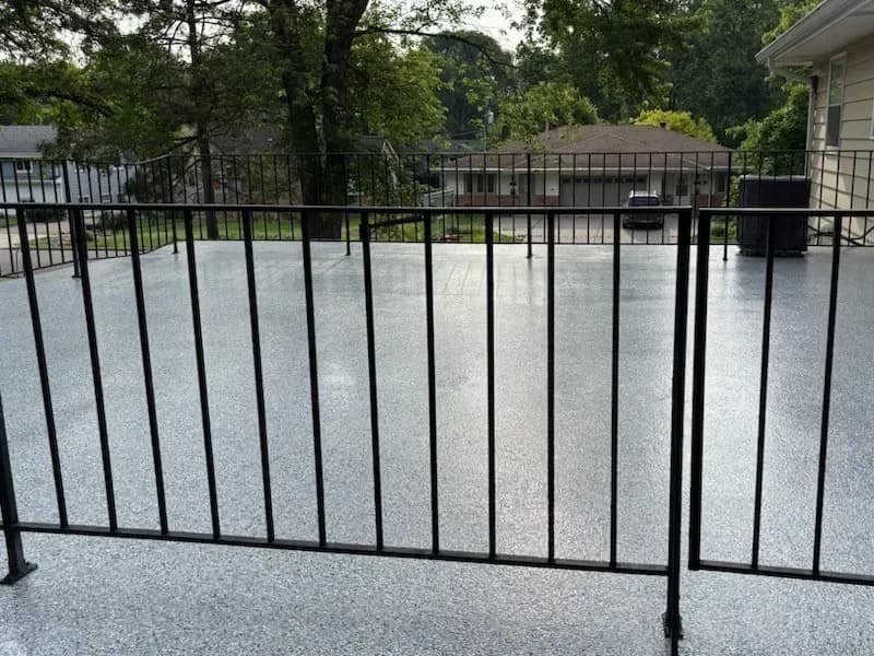 A gray flecked concrete coated flooring patio with a black metal fence around it.