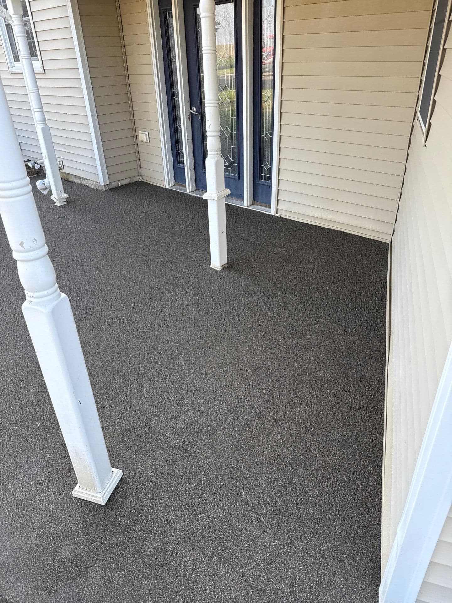 A tan house with blue entry door and newly-coated dark gray Resist front patio.