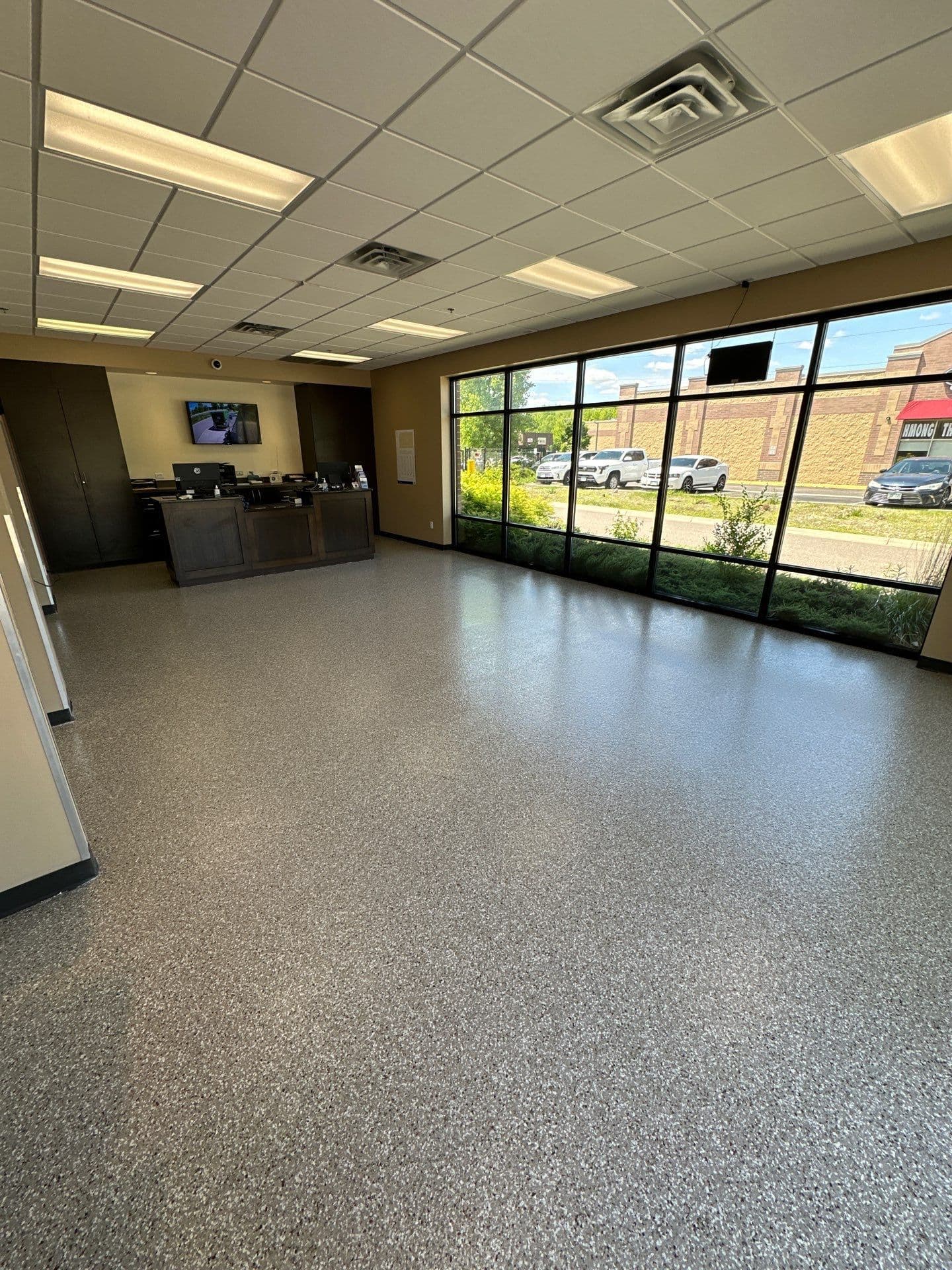 A commercial retail storefront with large windows and newly-coated gray flecked concrete flooring.