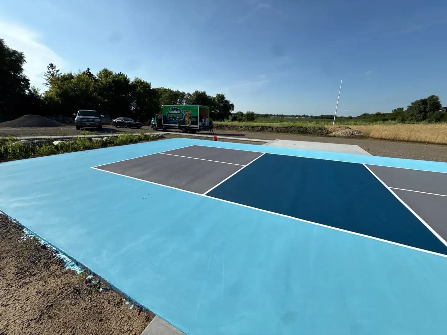 A newly-coated gray, blue, and white outdoor pickleball concrete flooring court.